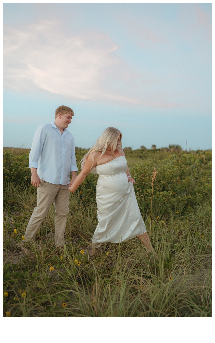 couple holding hands and walking through the brush at sebastian inlet beach during sunrise