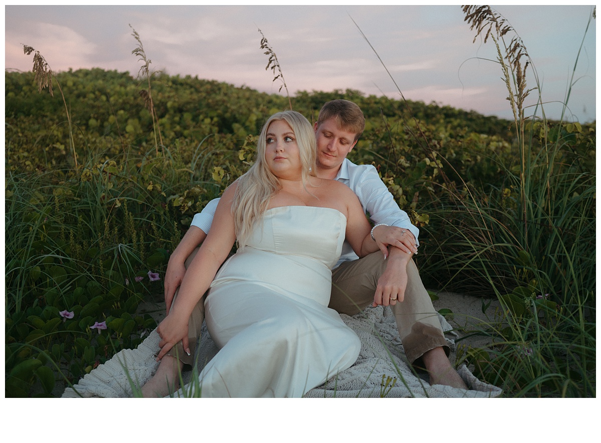 groom and bride sitting within berm while groom kisses brides temple after florida beach elopement