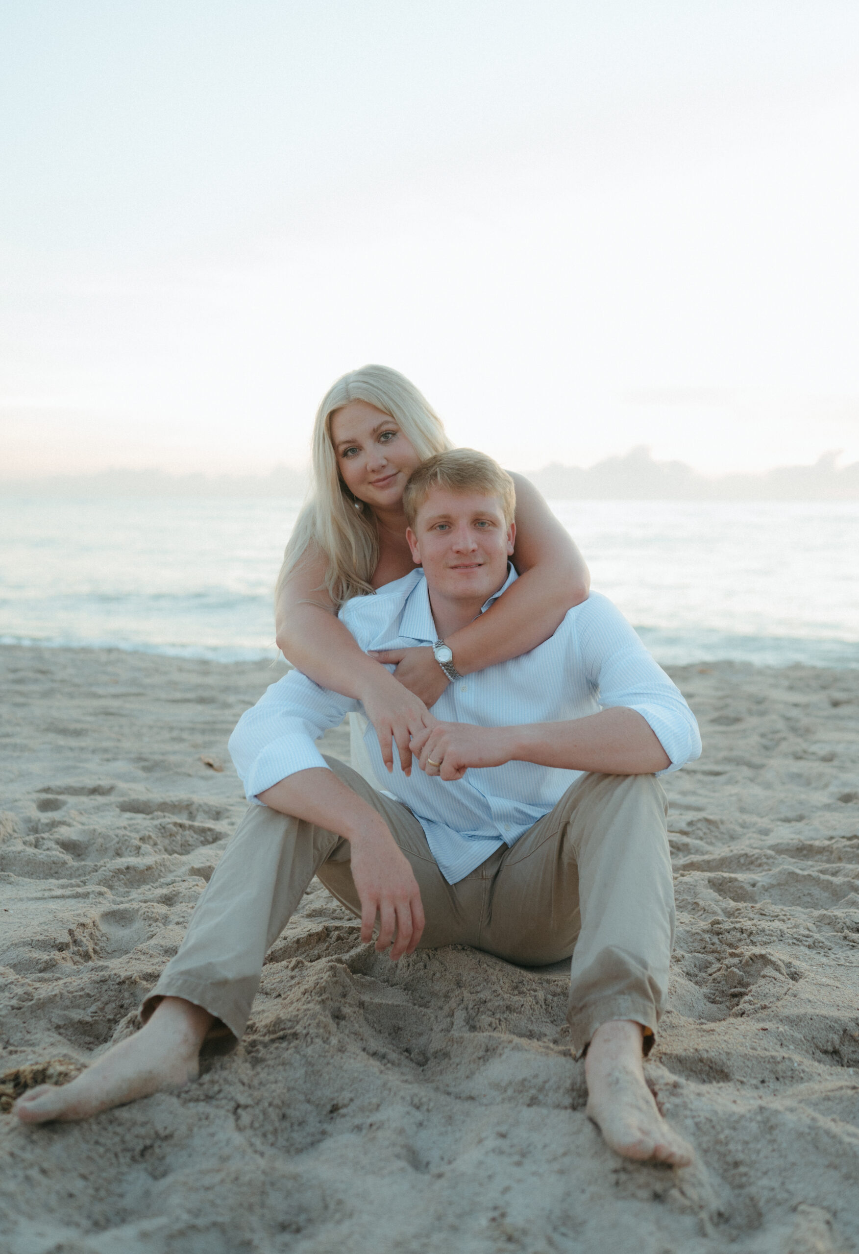 bride embracing groom on florida beach while sitting on the sand at sebastian inlet beach