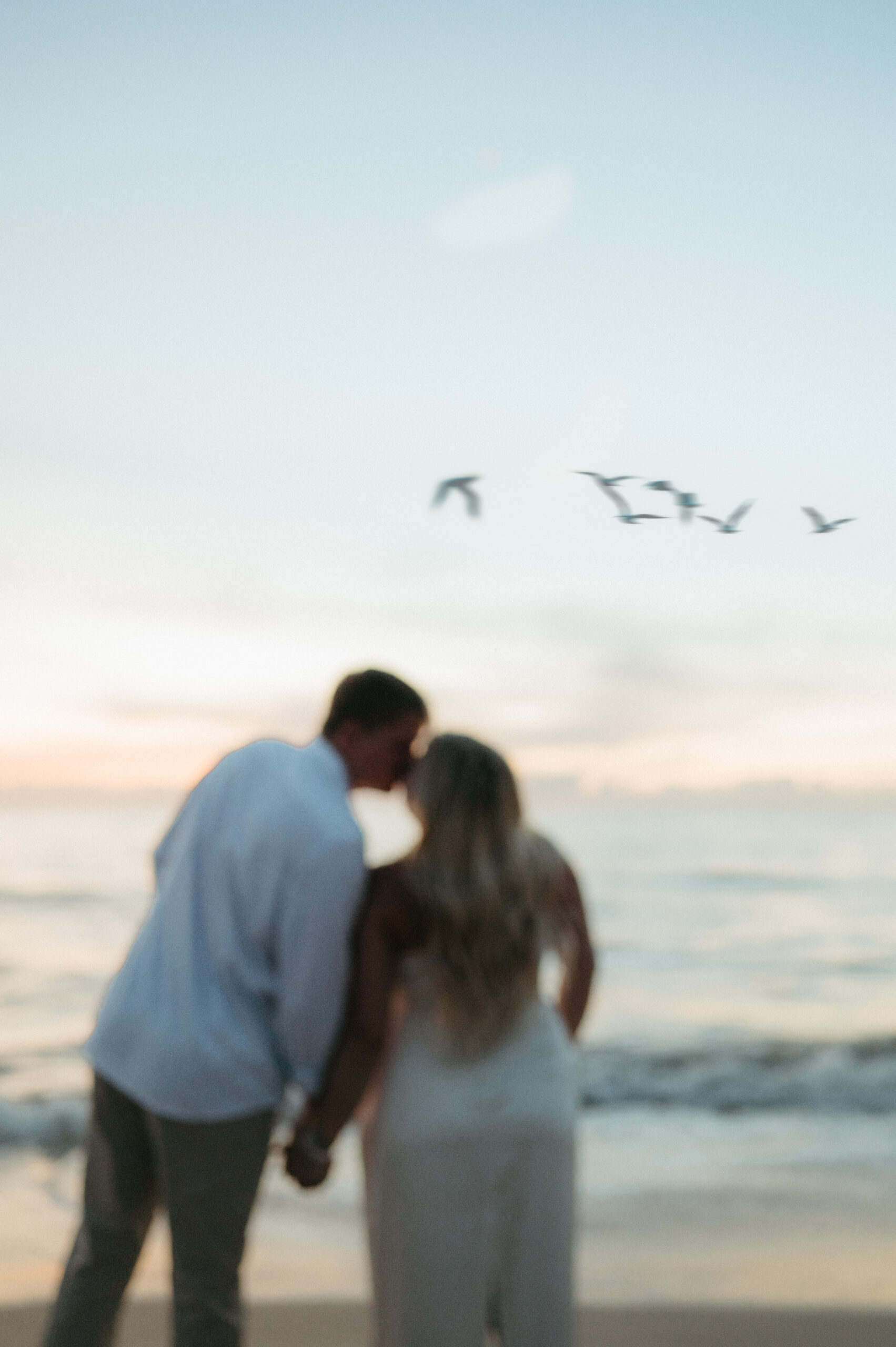 unique bride and groom facing the sunrise and kissing while seagulls fly across the sky during sebastian inlet elopement