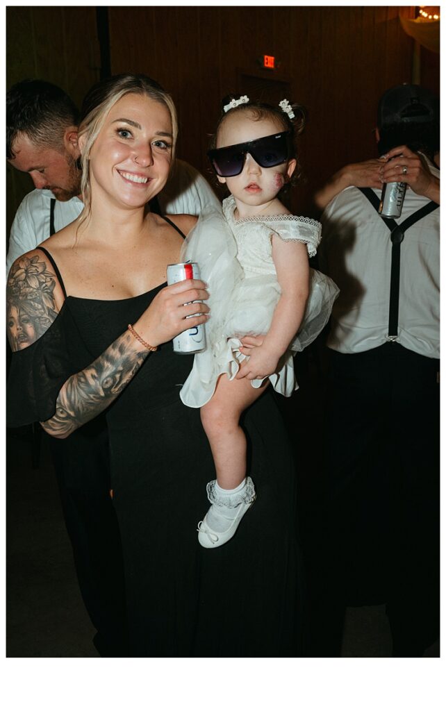 bridesmaid holding fun flower girl with sunglasses on during reception