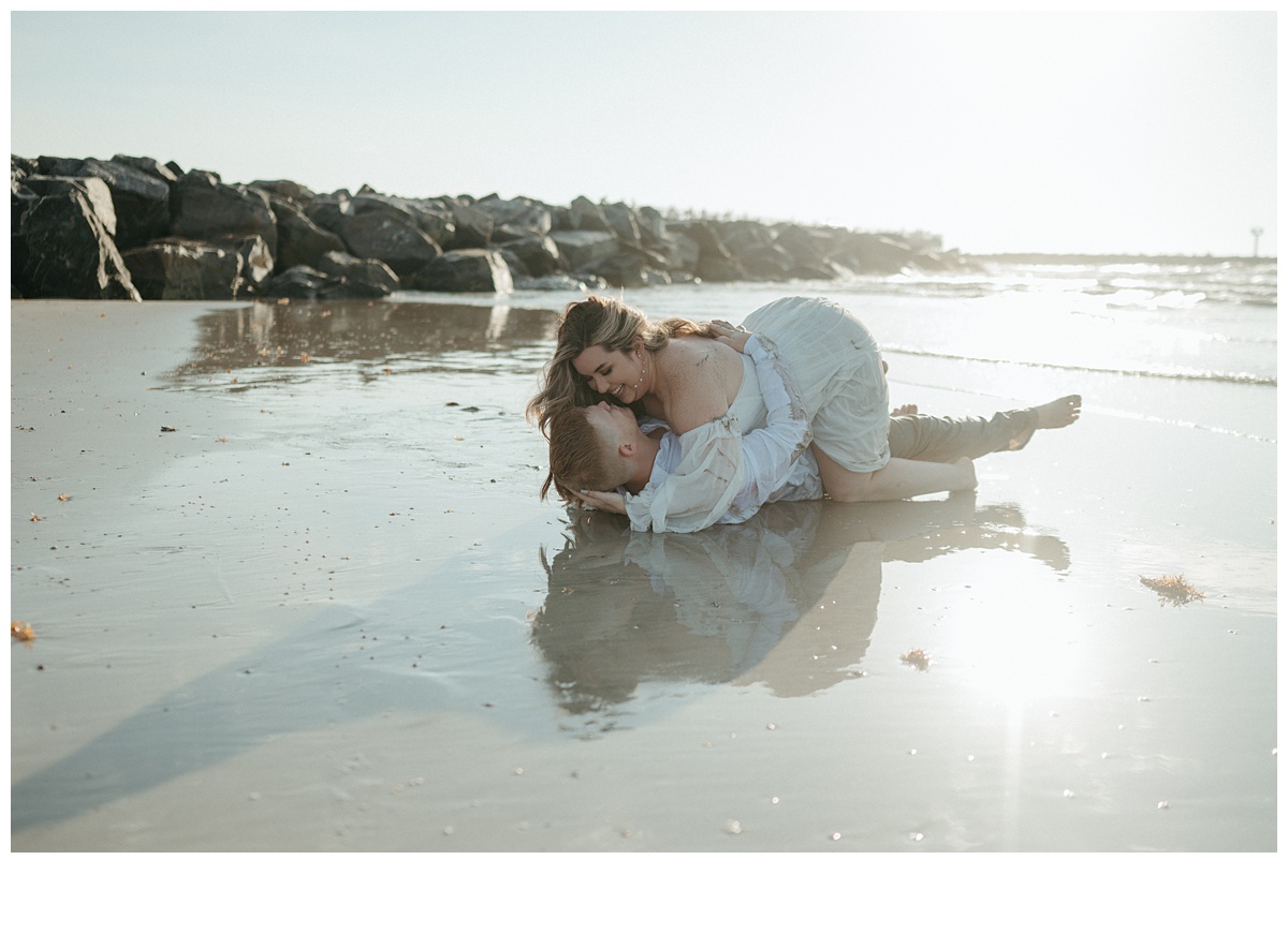 bride and groom rolling around on the beach