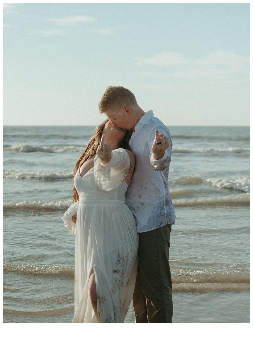 bride and groom kissing on the beach with ring fingers displayed