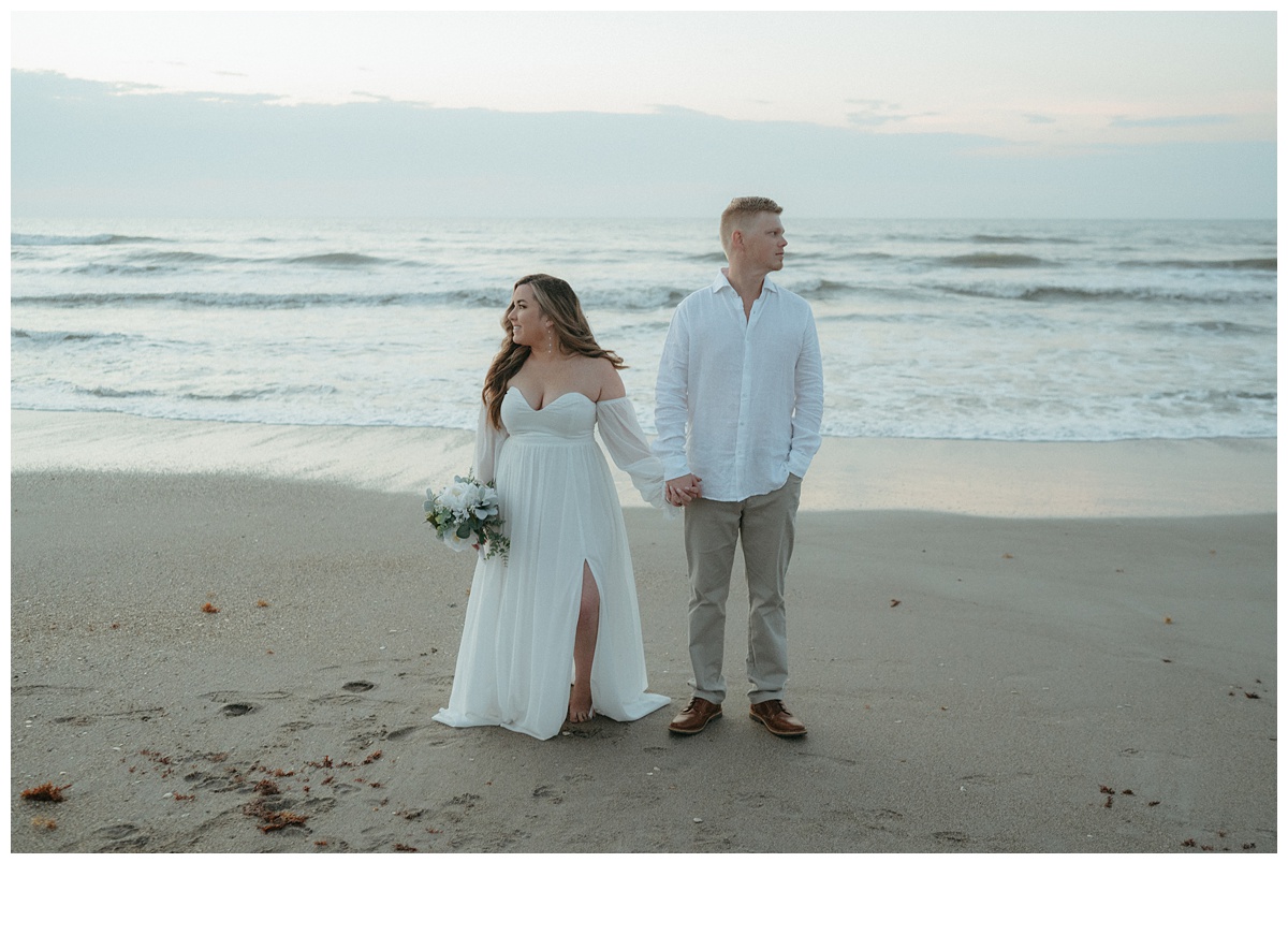 bride and groom hold hands on beach looking in opposite directions