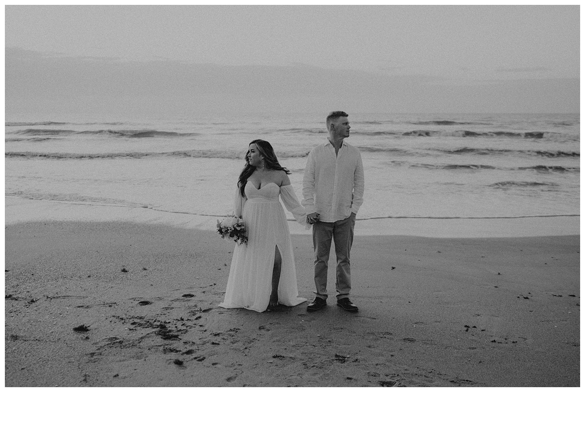 black and white bride and groom hold hands on beach looking in opposite directions