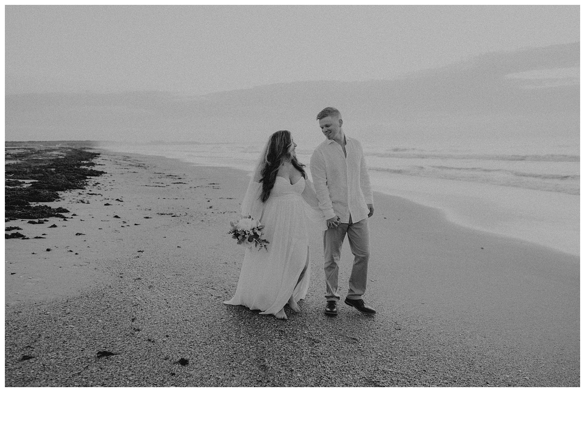 black and white bride and groom looking at each other while walking on beach