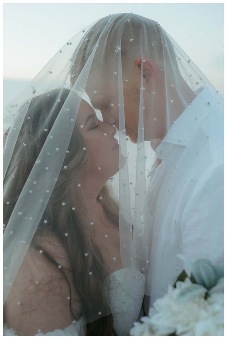 bride and groom intimate photo nose to nose under pearl veil.