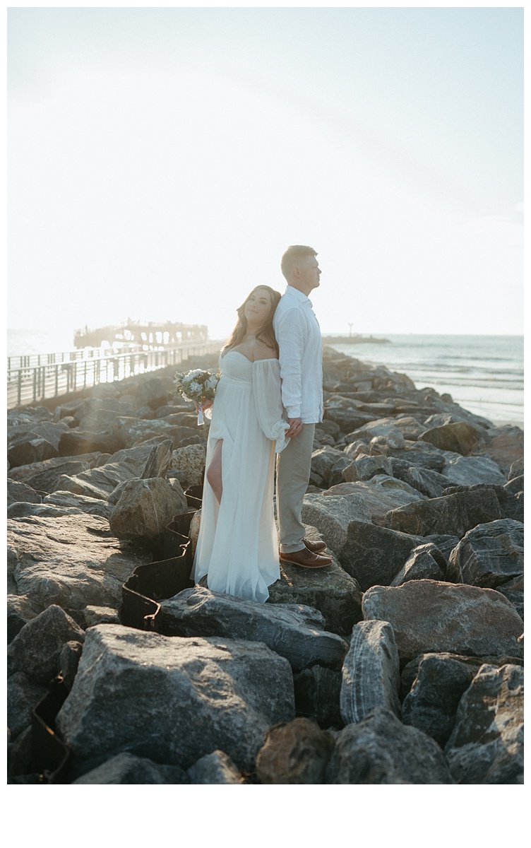 bride and groom back to back on jetty rocks at beach