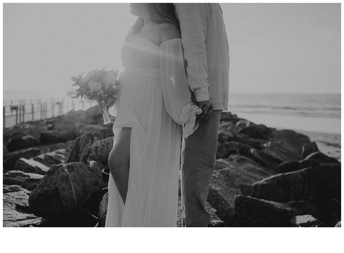 black and white holding hands on jetty rocks at beach