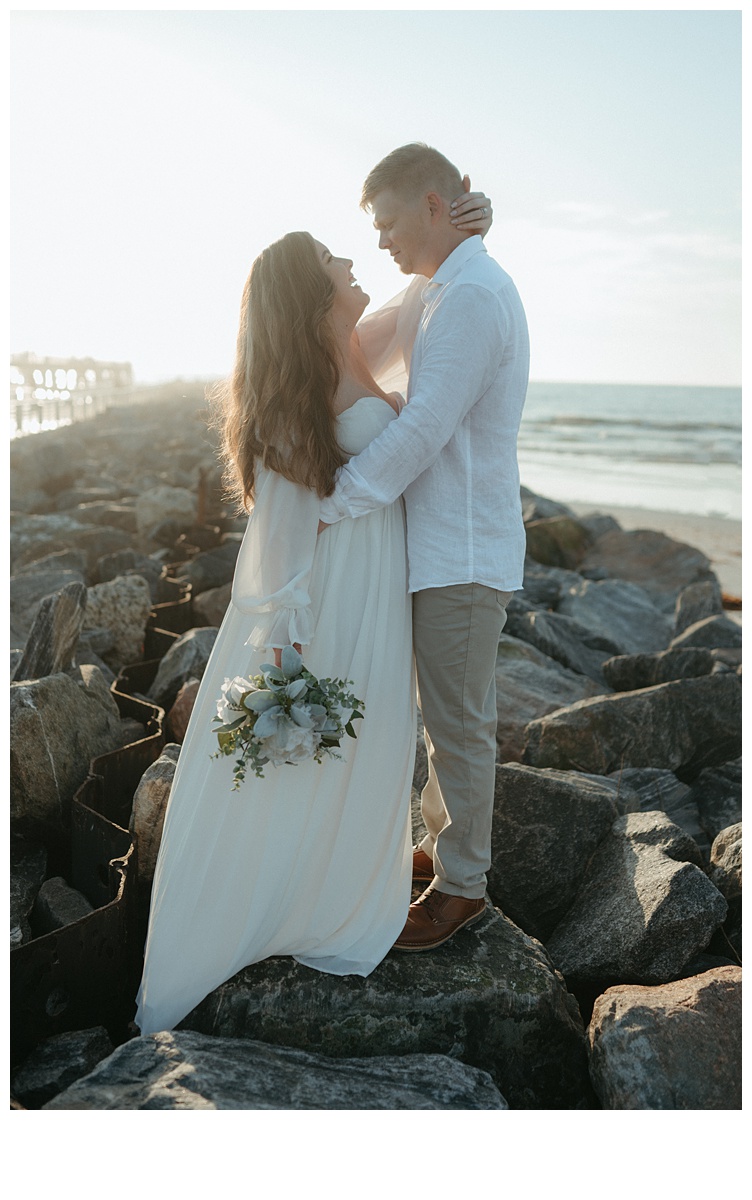 bride and groom standing face to face on rocks at beach