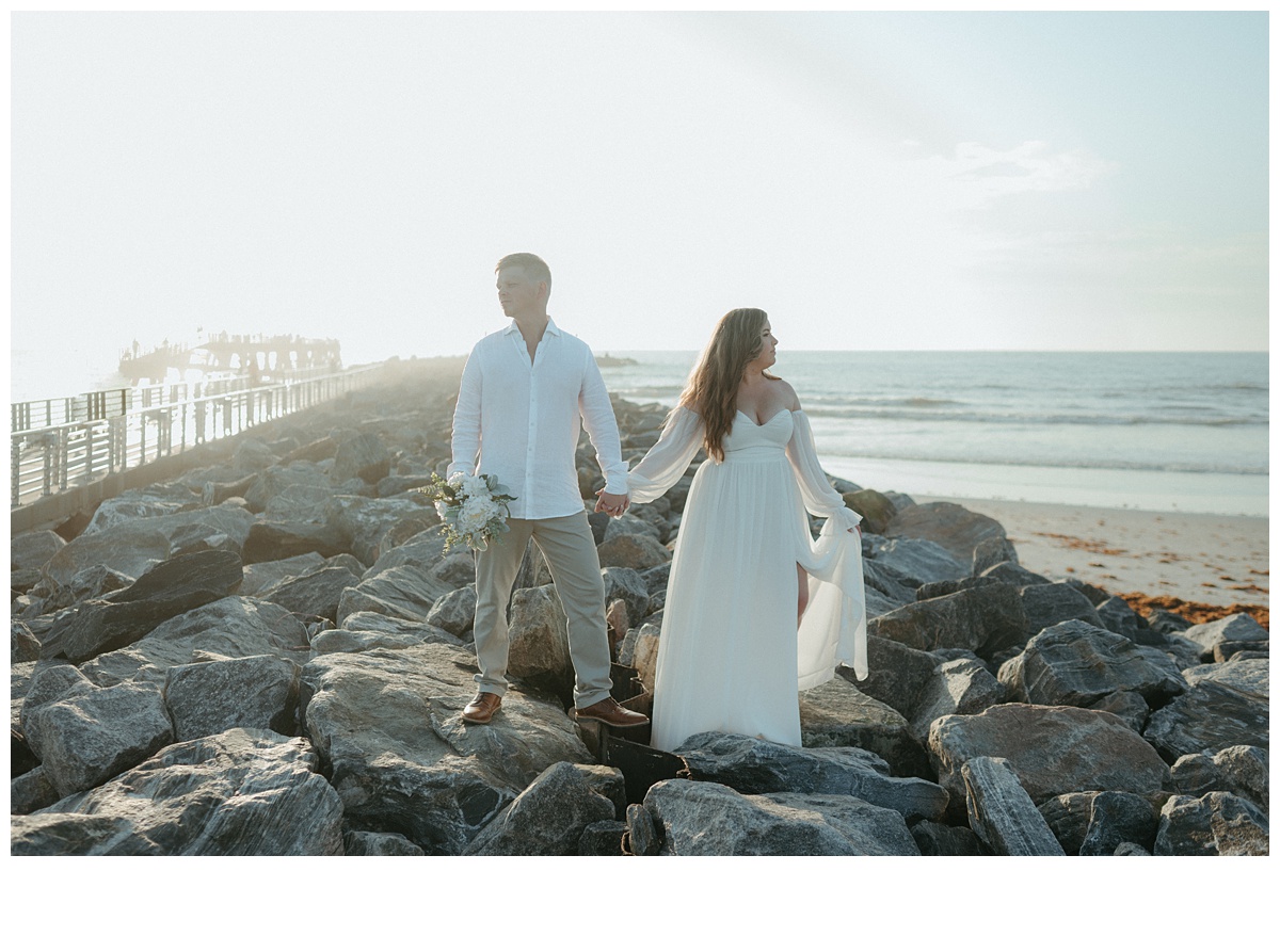 grom holding bouquet while couple looks in opposite directions on jetty rocks