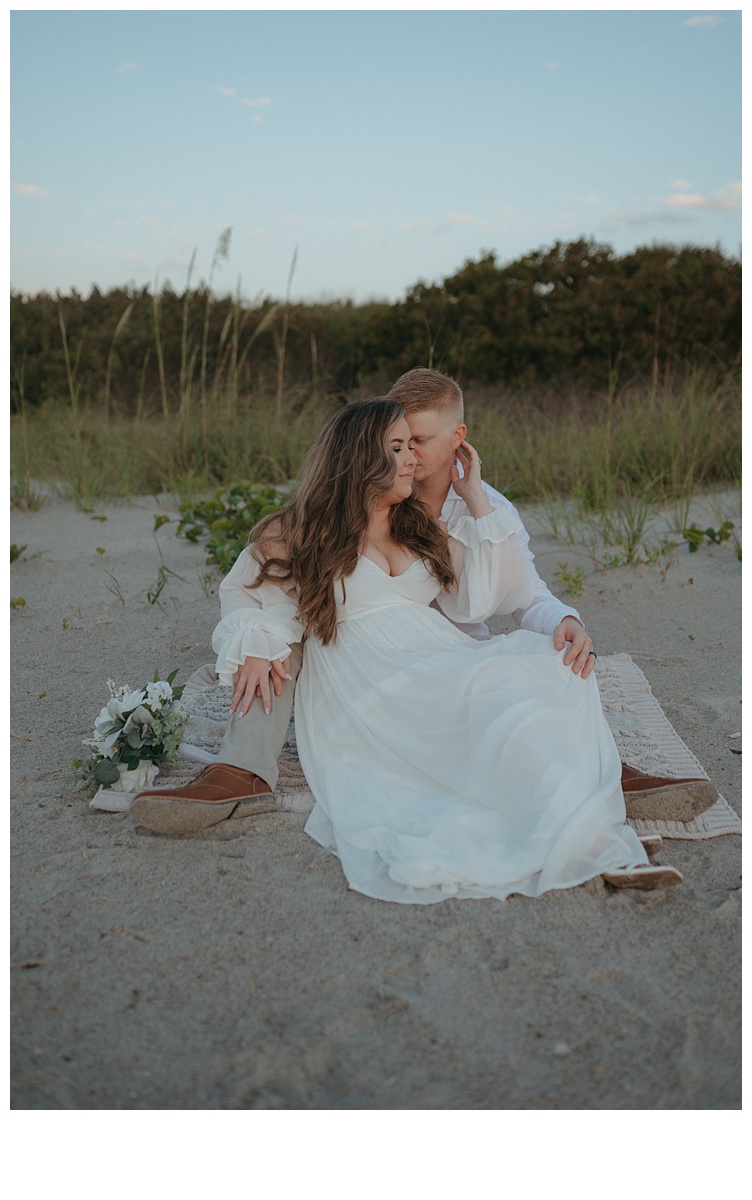 intimate moment between bride and groom sitting on sand at the beach