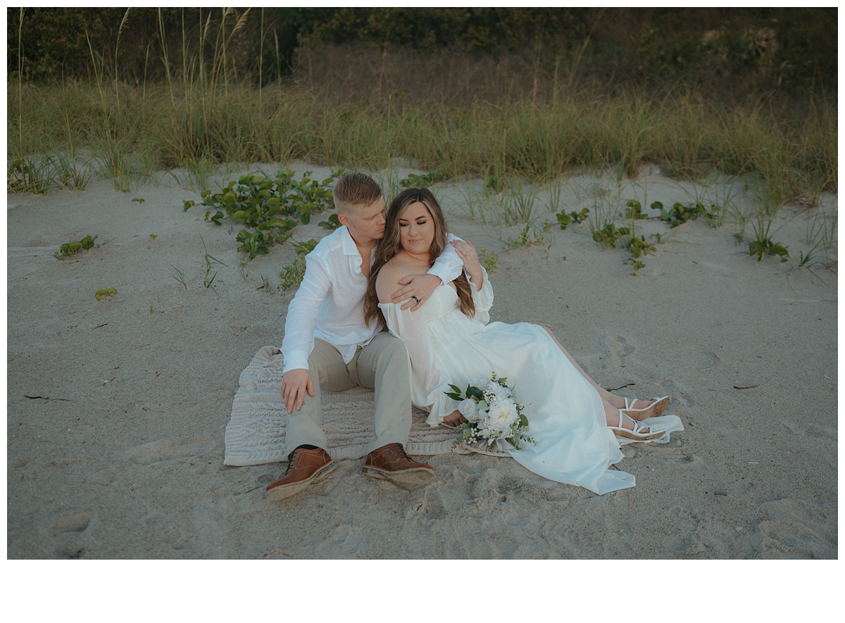 bride and groom sitting on the sand at the beach