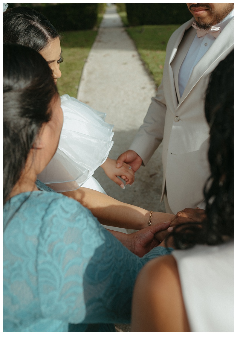 parents holding bride and grooms hand during prayer moment