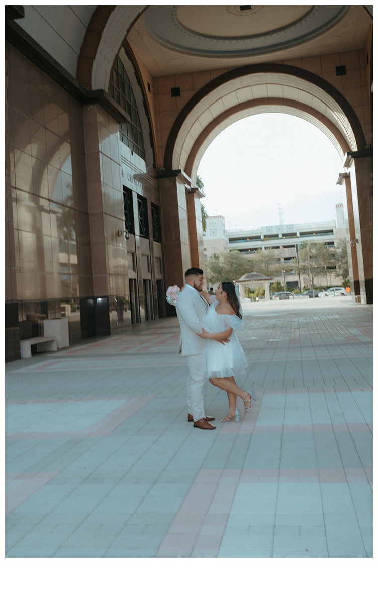 bride and groom fun embrace under courthouse arch in downtown palm beach