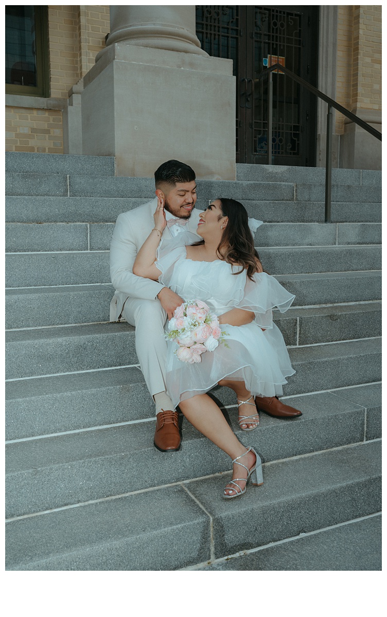 intimate flash photo of bride and groom sitting on steps while smiling at each other.