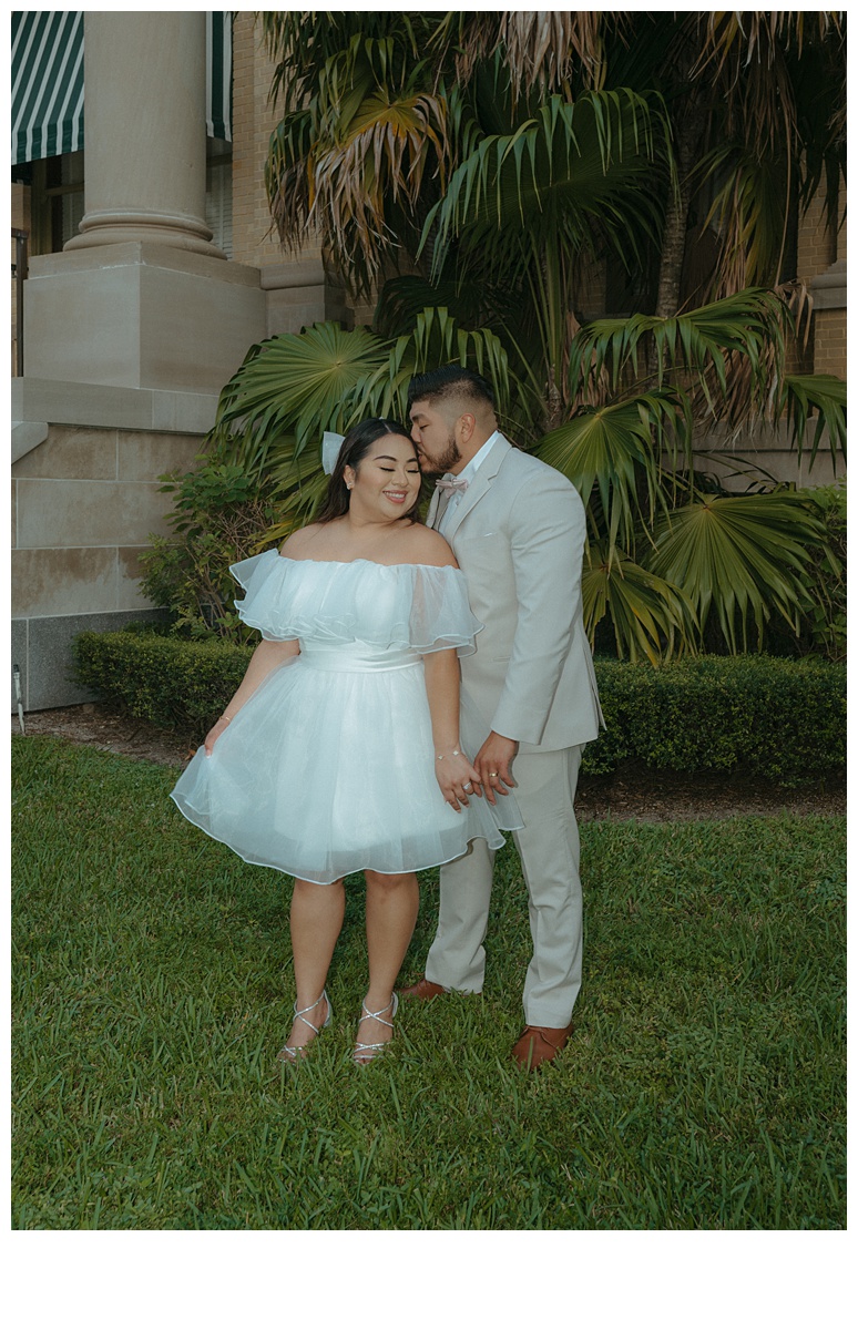 bride and groom hold hands while groom kisses top of bride head