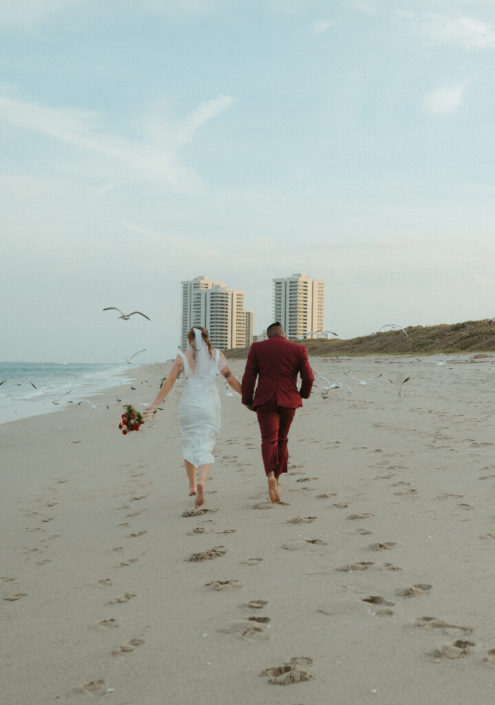 Bride and groom running on the beach in Florida with seagulls flying in the air