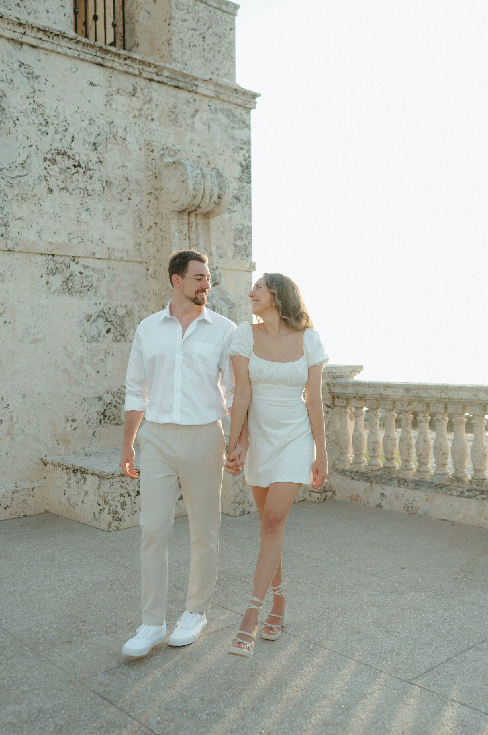 Girl in a short white dress holding her partners hand. Man wearing tan pants and a white t-shirt in Palm Beach Island