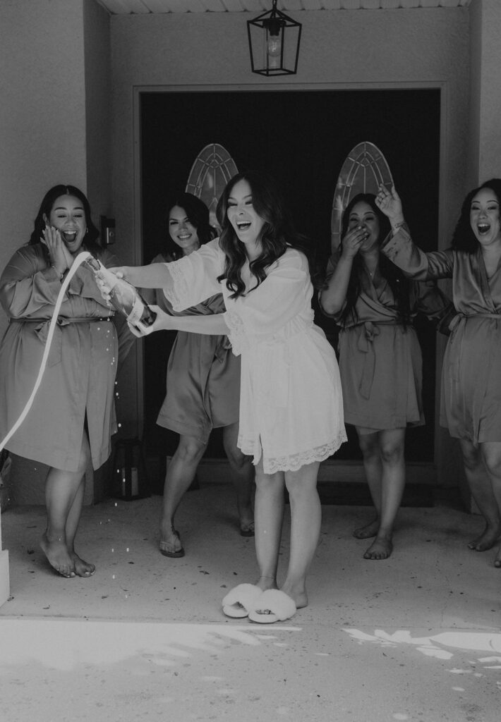 bride popping a bottle with her bridesmaids before her wedding